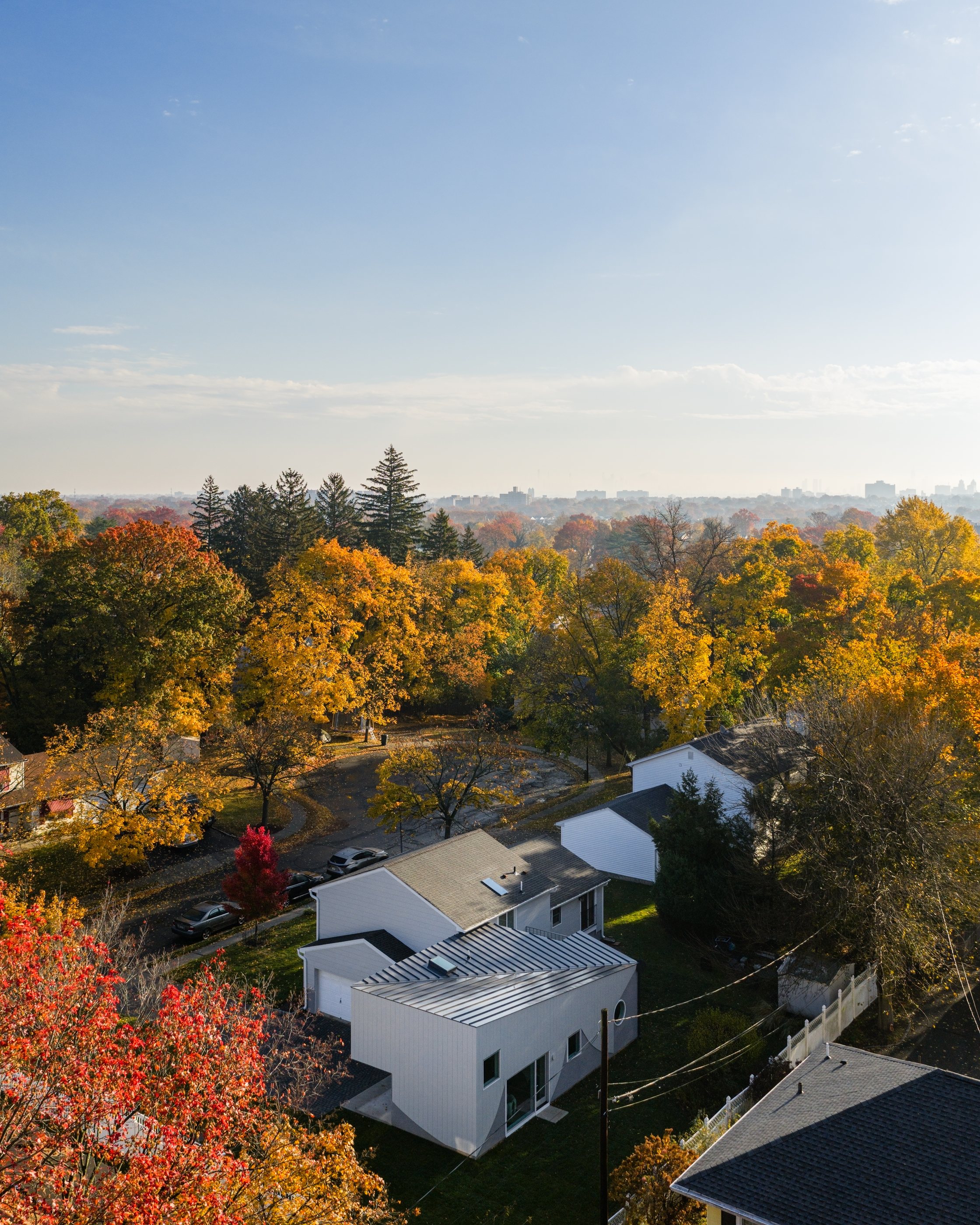 Aerial view of the Swoop ADU behind the existing split-level house, set in a cul-de-sac of mid-century homes among autumn trees in South Orange, NJ