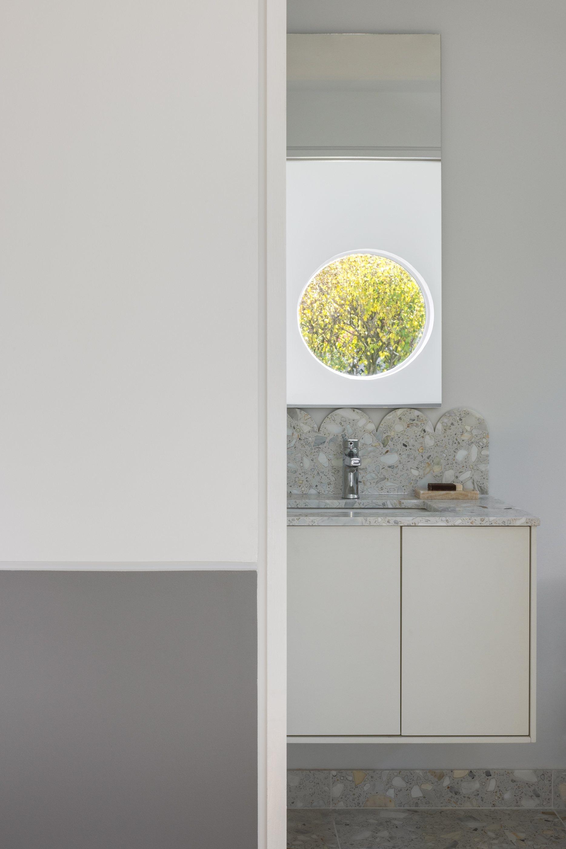 The Swoop ADU bathroom vanity in terrazzo with a round porthole window above the sink