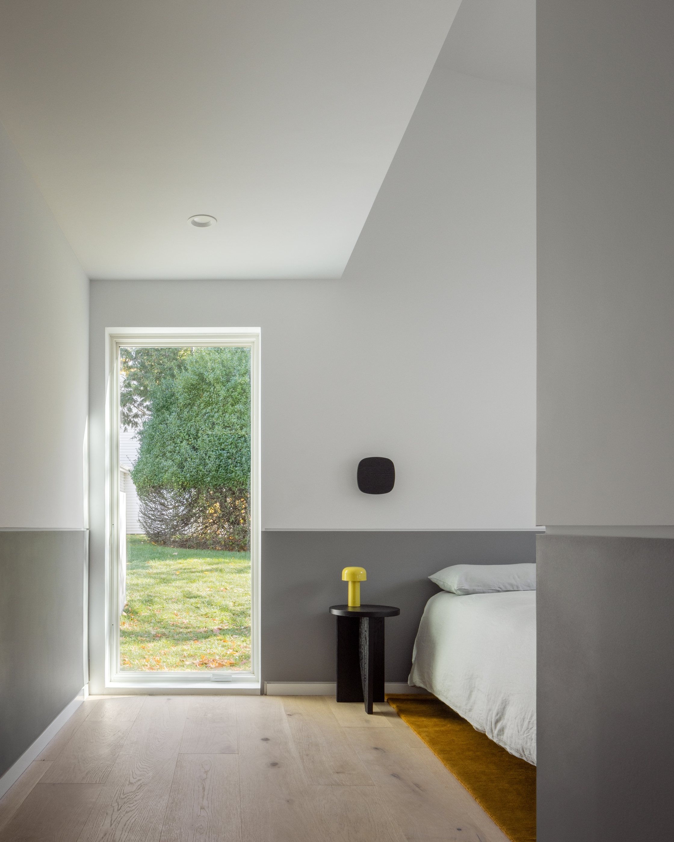 The Swoop ADU primary bedroom with a full-height window onto the garden and a two-tone gray-and-white wall