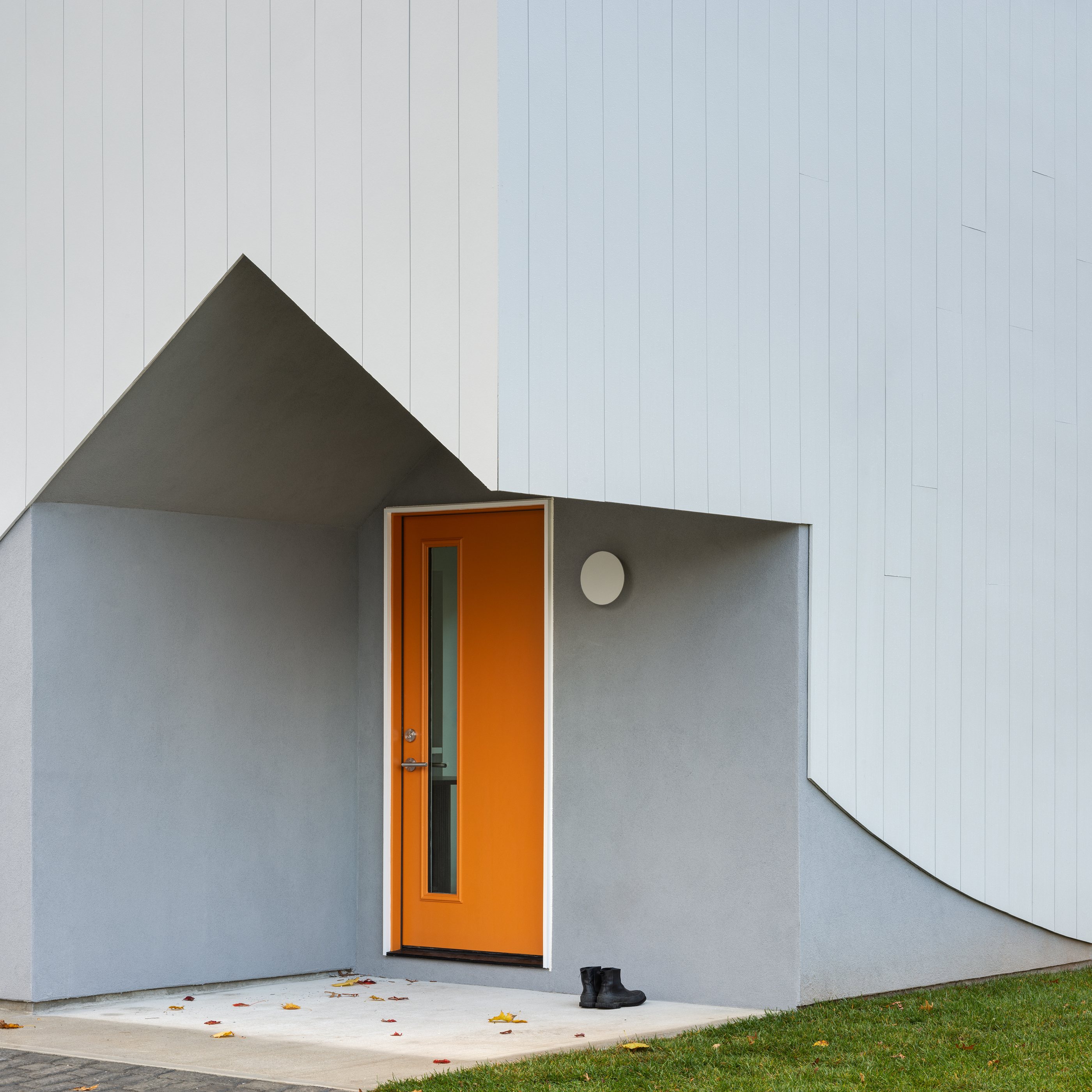 The Swoop ADU's bright orange front door set under a gabled porch carved into the curved facade