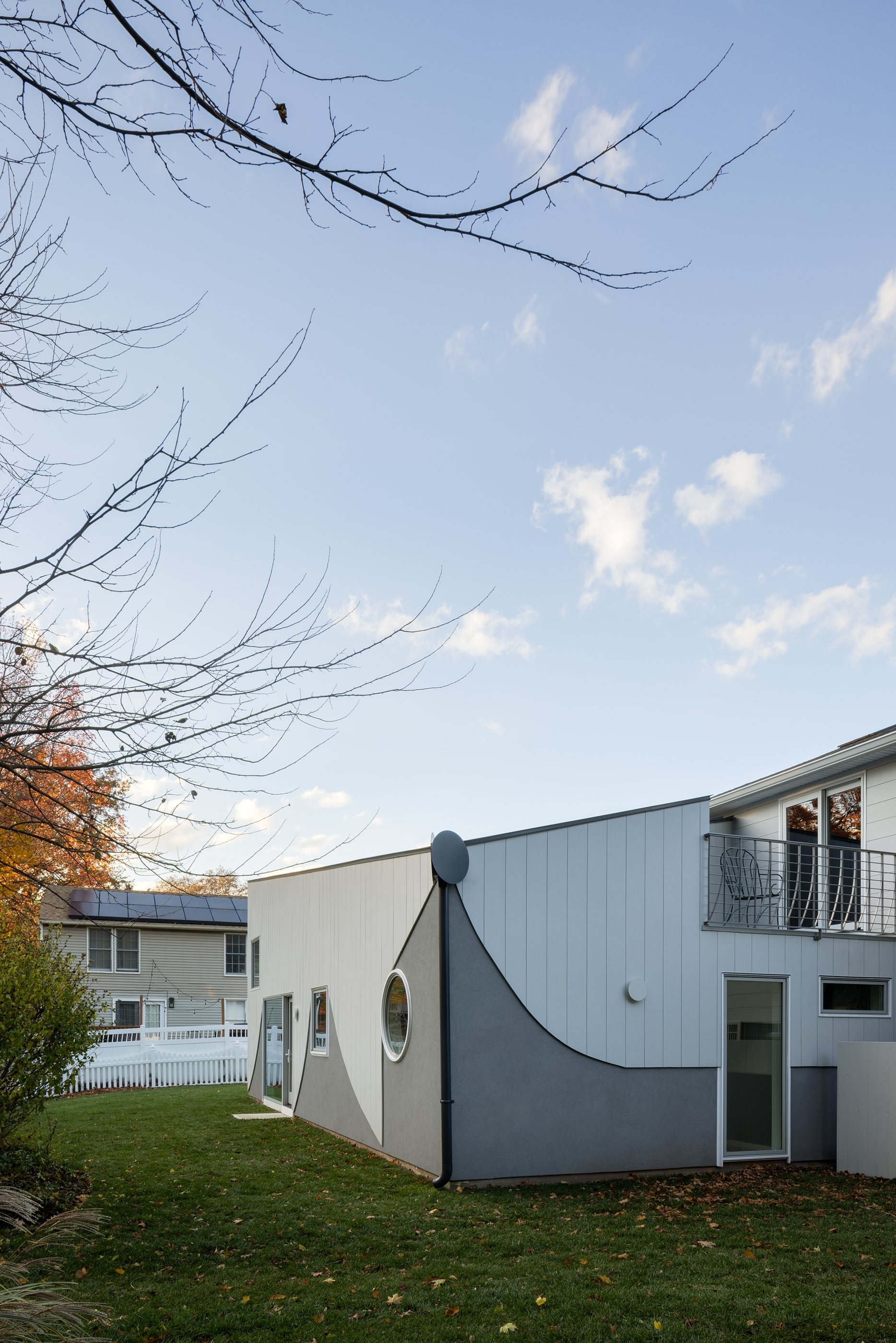 The Swoop ADU's curved fiber-cement facade with its porthole window and sliding doors, beside the existing split-level