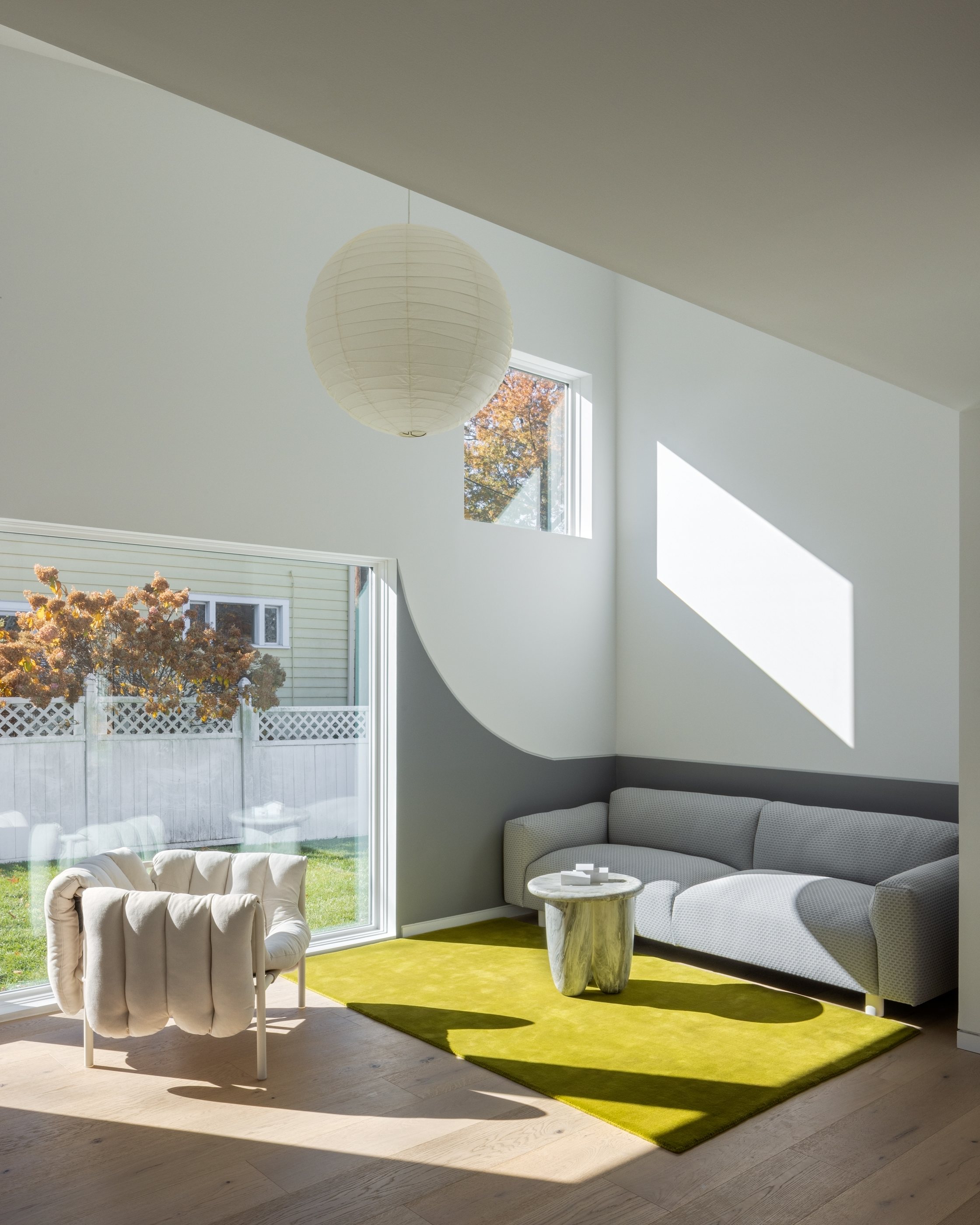 The Swoop ADU living room: a vaulted ceiling, full-height sliding doors to the backyard, a green rug and a gray sofa