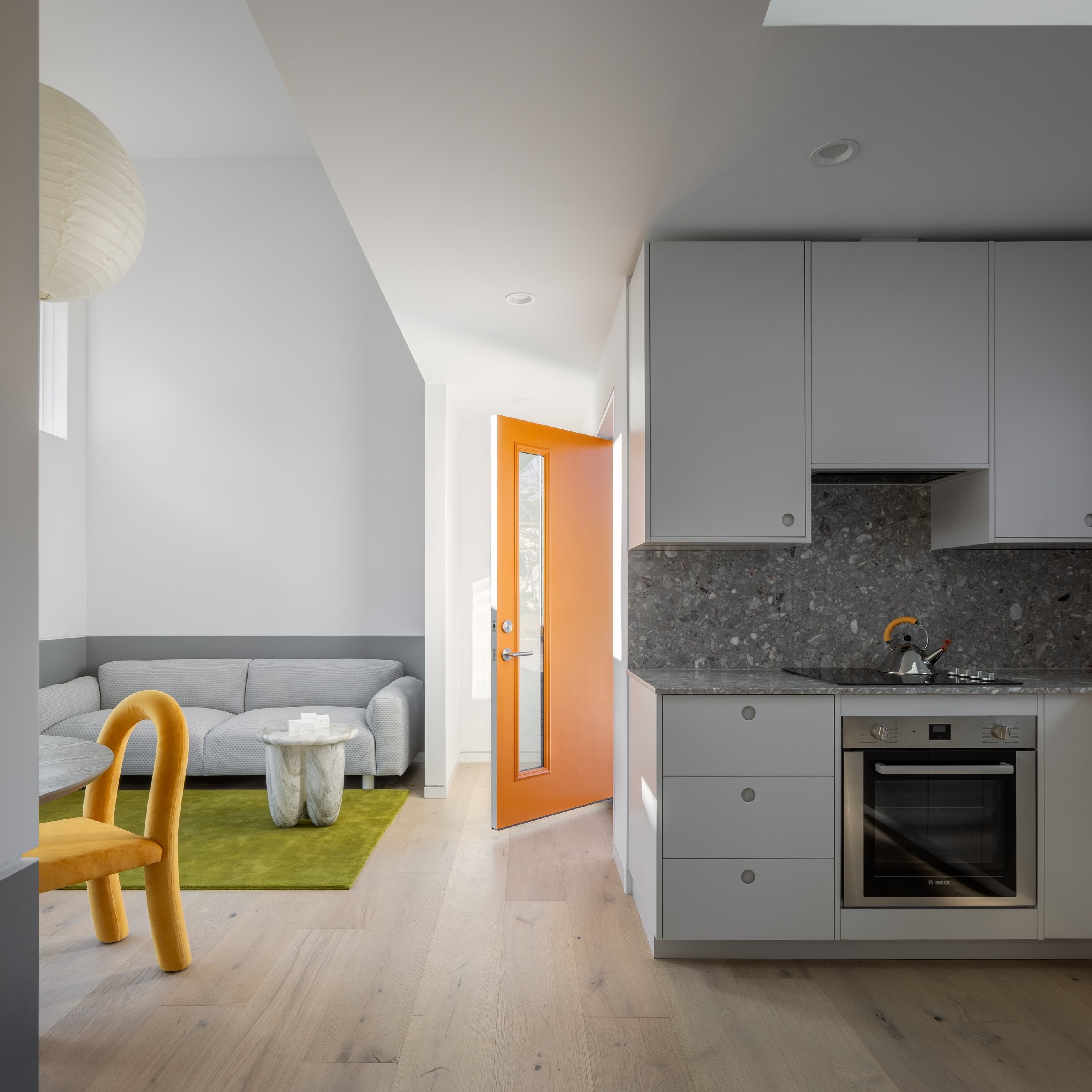 The Swoop ADU's open-plan interior: a gray kitchen at right, living area with a green rug and the orange front door beyond